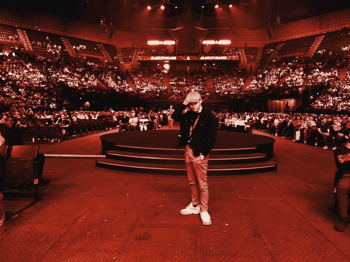 Joakim standing on the floor of a large esports arena, the crowd behind him, toned red.