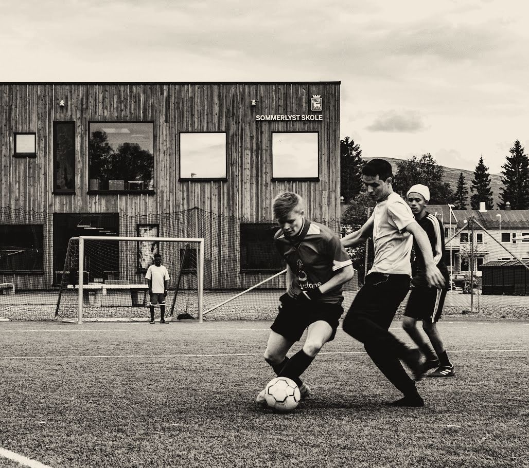 Black-and-white photo of Joakim dribbling a football past a defender on an artificial pitch.