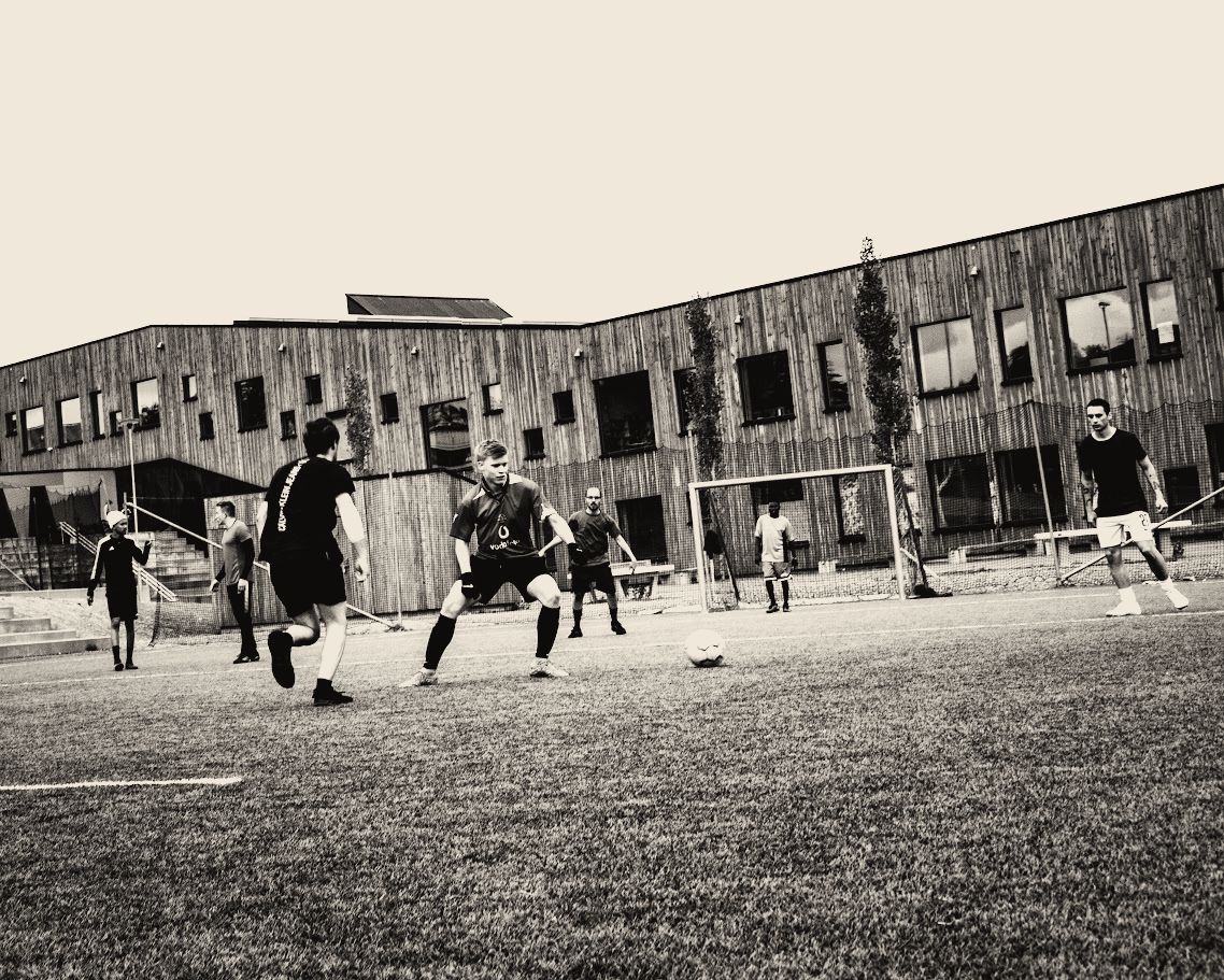 Black-and-white wide shot of a football match on a school pitch in Tromsø.