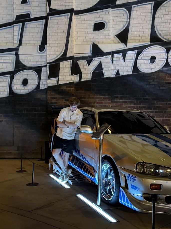 Joakim leaning on the silver and blue Nissan Skyline R34 from Fast and Furious, in front of a Hollywood mural at Universal Studios Hollywood.