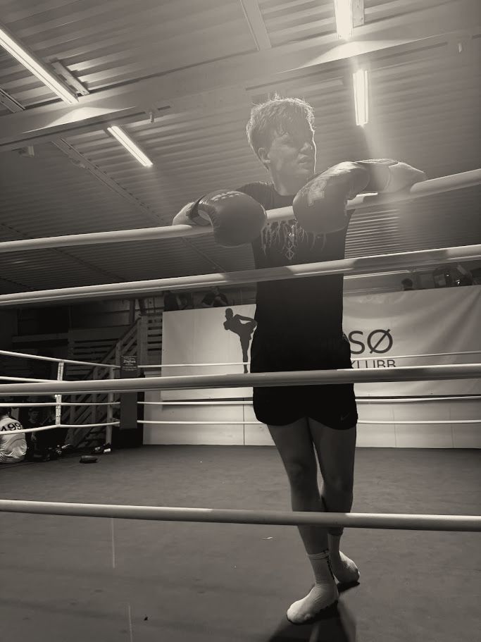 Joakim leaning on the ropes of a kickboxing ring in Tromsø, gloves on, black and white.