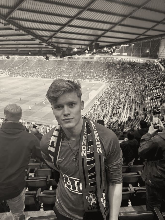 Joakim at Old Trafford in a red shirt and scarf, the pitch behind him.