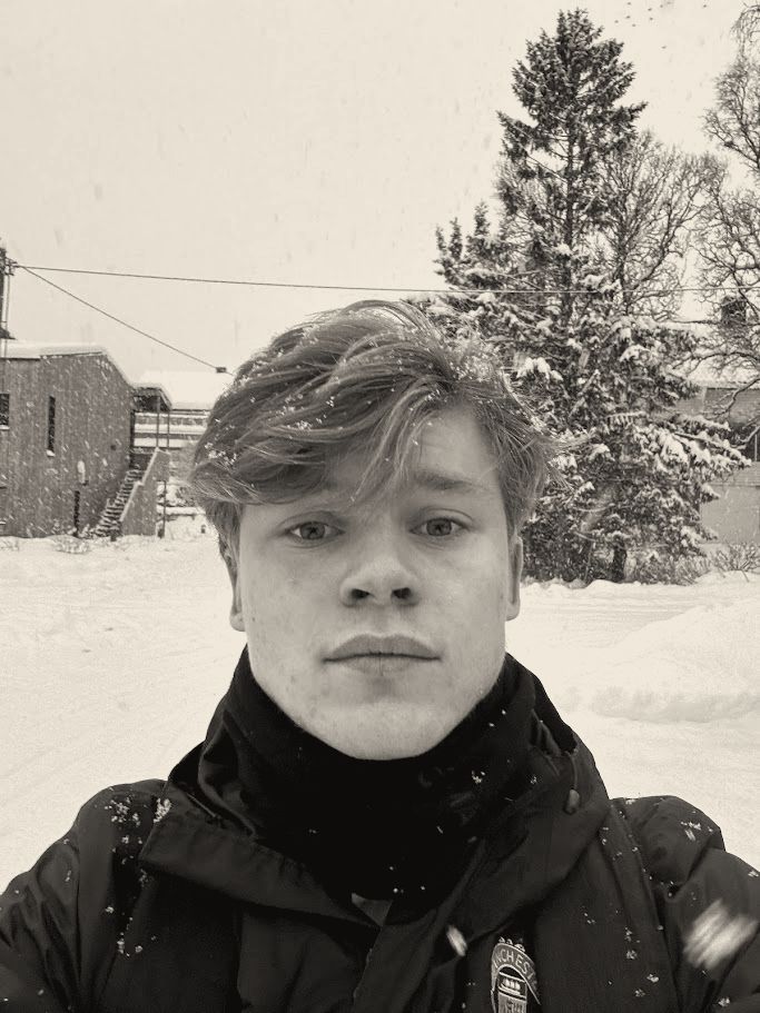 Close-up selfie of Joakim in the snow in Tromsø, snow-covered trees behind.